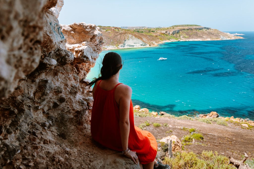 Girl looking out to blue water from a cave on Gozo Island